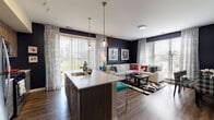 Located at 2100 Haddonfield Rd in Pennsauken, NJ, this single-floor residence offers a thoughtfully designed open-concept layout that seamlessly connects the kitchen, dining, and living areas. The kitchen is a standout feature, boasting a large center island with a white quartz countertop, dark wood cabinetry, stainless steel appliances, track lighting, and globe pendant lights. Teal bar stools add a vibrant pop of color that carries through the home's design palette.

The living area is anchored by a bold dark accent wall, wide-plank hardwood flooring, and large windows dressed with patterned curtains that fill the space with natural light and provide outdoor views. A welcoming hallway connects the main living space to the private quarters, featuring warm multi-toned walls and decorative accents.

The bedrooms are carpeted for comfort and highlight striking teal accent walls paired with large windows that let in generous natural light. The primary bedroom includes a seating area and exterior views. The bathroom features teal walls, wood-look flooring, a tub-shower combination, and framed wall art, completing the home's cohesive modern aesthetic throughout.