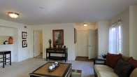 This single-floor residence offers a warm and functional layout designed for comfortable everyday living. The living area serves as the heart of the home, featuring plush wall-to-wall carpeting that adds a sense of coziness underfoot. Neutral white walls provide a clean, versatile backdrop that complements a variety of furnishing styles. The room is anchored by a wooden coffee table and accented with a decorative console table displaying curated décor, lending the space a classic, lived-in charm. A framed piece of artwork adds a touch of personality to the walls, while a ceiling-mounted light fixture provides ambient illumination. Classic six-panel doors open to connecting rooms, hinting at a well-connected floor plan that flows naturally from one space to the next. The overall ambiance is understated and inviting, with a traditional aesthetic that prioritizes comfort and practicality. The measured, open arrangement of the living area allows for flexible furniture placement, making it easy to personalize the space to suit a range of lifestyles.