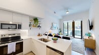 Located at 2585 Spruce Ave in West Palm Beach, FL, this thoughtfully designed one-bedroom, one-bathroom residence offers a clean, modern aesthetic throughout its efficiently utilized single-floor layout. Soaring ceilings amplify the sense of space in the open-concept living and kitchen area, where natural light pours in through large sliding glass doors that lead to a private balcony overlooking lush greenery. The living room features light wood flooring, crisp white walls, and wall sconces that complement the airy, contemporary atmosphere.

The kitchen is outfitted with flat-panel white cabinetry extending to the ceiling, stainless steel appliances, a white quartz countertop, an undermount sink, and an island that doubles as a dining and prep surface. Open shelving adds a stylish, functional touch.

The bedroom is generously proportioned with its own walk-in closet featuring built-in shelving and high ceilings that continue the spacious feel of the home. A large window frames views of the surrounding landscape, filling the room with natural light.

The bathroom offers a sleek single vanity with white cabinetry, a large mirror, quartz countertop, a glass-enclosed shower, and in-unit washer/dryer access. Light wood flooring ties the space together cohesively.
