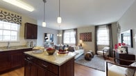 Located in Kingswood, this single-floor residence showcases a thoughtfully designed open-concept layout that seamlessly connects the kitchen, dining, and living areas into one cohesive and inviting space. The kitchen is appointed with rich dark wood cabinetry, a granite-topped island with pendant lighting overhead, and a classic subway tile backsplash — combining elegance with everyday functionality. The island serves as a natural gathering point, offering both prep space and a casual place to entertain. Flowing directly from the kitchen, the dining area provides a dedicated space for meals, framed by a contemporary chandelier. The living room is generously proportioned, featuring warm hardwood flooring, a plush area rug, and a comfortable seating arrangement that invites relaxation. Multiple large windows allow abundant natural light to fill the space throughout the day, creating a bright and airy atmosphere. Neutral wall tones complement the warm wood accents and provide a versatile backdrop for a variety of décor styles. The overall ambiance of this home is modern yet welcoming, with a well-balanced combination of refined finishes and functional design that suits both daily living and entertaining.