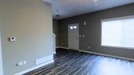 This 3-floor property presents a clean, contemporary interior defined by a cohesive neutral color scheme. The main level entry area is immediately welcoming, showcasing dark, wide-plank hardwood-style flooring that contrasts sharply with crisp white baseboards and trim, creating a polished, modern aesthetic. The walls are finished in a warm charcoal-gray tone that lends the space a grounded, sophisticated atmosphere.

The front entryway features a classic paneled white door with glass accent panels at the top, allowing natural light to filter into the space. A window on the adjacent wall further supplements the natural light, brightening the otherwise moody interior palette. Flush-mount ceiling lighting provides additional illumination throughout the open area.

White baseboard heating units line the lower walls, indicating a functional heating system integrated seamlessly into the design. The open layout of the entry and main living area offers a generous sense of space, with clear sightlines that enhance the feeling of roominess. The staircase visible at the edge of the frame hints at the additional levels above, suggesting ample living space distributed across all three floors of this well-appointed property.
