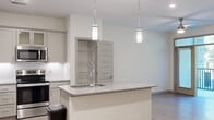 Located at 206 S Collegiate Dr in Surf City, NC, this single-floor unit offers a clean, contemporary design with a bright and open layout. The kitchen serves as a central highlight, featuring gray shaker-style cabinetry with frosted glass upper panels, granite countertops, a subway tile backsplash, and a large center island with a built-in sink illuminated by sleek pendant lighting. Stainless steel appliances, including a refrigerator, microwave, and range, complete the kitchen's modern aesthetic. The open-concept floor plan connects the kitchen seamlessly to the living area, which is finished with light wood-look flooring and ceiling fan, and leads to a private balcony that brings in natural light and outdoor views. A dedicated pantry closet adds convenient storage off the kitchen. The bedrooms are carpeted for comfort, each featuring panel-style doors, ceiling fans, and windows that invite natural light. The bathroom is well-appointed with granite countertops, gray cabinetry, a large vanity mirror, and light wood-look flooring. A laundry area with washer and dryer connections is also included. Throughout, the neutral color palette and consistent finishes create a cohesive, modern living environment.
