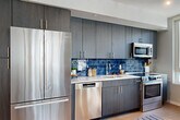 Located at 1771 N Pierce St in Arlington, VA, this well-appointed two-bedroom, two-bathroom residence offers a thoughtfully designed single-level floor plan. Light wood flooring flows throughout, complemented by recessed lighting and a neutral color palette that creates a bright, cohesive atmosphere.

The open-concept living and dining area is a standout feature, anchored by large floor-to-ceiling windows that flood the space with natural light and provide views of the surrounding neighborhood. A structural column adds an architectural touch to the living area, which flows seamlessly into the dining space and out to a private balcony.

The kitchen is outfitted with dark wood cabinetry extending to the ceiling, a striking deep-blue glazed tile backsplash, light quartz countertops, and a full suite of stainless steel appliances including a French-door refrigerator, dishwasher, microwave, and range.

The primary bedroom is generously sized with large windows offering city views. Both bathrooms feature modern vanities with bold cabinetry — one with a lighted mirror and tile flooring, the other with a tiled tub-shower surround. Three closets and a dedicated laundry area provide excellent storage. The welcoming hallway entry, adorned with recessed lighting, completes this polished and functional residence.