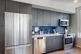Located at 1771 N Pierce St in Arlington, VA, this well-appointed two-bedroom, two-bathroom residence offers a thoughtfully designed single-level floor plan. Light wood flooring flows throughout, complemented by recessed lighting and a neutral color palette that creates a bright, cohesive atmosphere.

The open-concept living and dining area is a standout feature, anchored by large floor-to-ceiling windows that flood the space with natural light and provide views of the surrounding neighborhood. A structural column adds an architectural touch to the living area, which flows seamlessly into the dining space and out to a private balcony.

The kitchen is outfitted with dark wood cabinetry extending to the ceiling, a striking deep-blue glazed tile backsplash, light quartz countertops, and a full suite of stainless steel appliances including a French-door refrigerator, dishwasher, microwave, and range.

The primary bedroom is generously sized with large windows offering city views. Both bathrooms feature modern vanities with bold cabinetry — one with a lighted mirror and tile flooring, the other with a tiled tub-shower surround. Three closets and a dedicated laundry area provide excellent storage. The welcoming hallway entry, adorned with recessed lighting, completes this polished and functional residence.