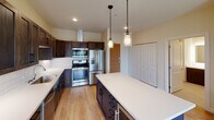 This single-floor unit presents a thoughtfully designed layout that balances functionality with modern aesthetics. Light hardwood flooring runs consistently throughout the space, contributing to a warm, cohesive feel across all areas.

The kitchen serves as a central highlight, showcasing rich, dark wood cabinetry paired with crisp white quartz countertops and a classic white subway tile backsplash. A generously sized center island provides additional workspace and casual seating. Stainless steel appliances, including a French door refrigerator, gas range, built-in microwave, and dishwasher, complement the space's contemporary design. Pendant lighting with glass fixtures hangs above the island, adding refined detail.

The living area is bright and open, benefiting from large sliding glass doors that lead to a private balcony, framing views of surrounding greenery and the neighborhood beyond. Exposed metallic ductwork runs along the ceiling, lending an industrial touch that contrasts interestingly with the unit's otherwise clean, neutral palette.

A bedroom features a standard window with similar outdoor views and access to a dedicated walk-in closet, which is equipped with wire shelving and hanging rods along multiple walls, offering well-organized storage capacity throughout.