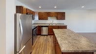 This 1-bedroom, 1-bathroom residence is designed with both functionality and comfort in mind, offering a cohesive single-floor layout that makes efficient use of every square foot. The kitchen serves as a standout feature, showcasing rich warm-toned cabinetry, stone-look countertops, and a full suite of stainless steel appliances including a refrigerator, range, microwave, and dishwasher. A central island provides additional prep space and casual seating, while recessed lighting overhead and durable hardwood-style flooring add a polished, modern touch throughout. The open layout allows the kitchen to connect naturally to the living area, enhancing the sense of space and flow. The bedroom is finished with plush carpet and features a dedicated closet with a full-width hanging rod, offering ample storage. The bathroom is clean and understated, with hardwood-style flooring, a bathtub, and neutral wall tones that create a calm, functional atmosphere. Recessed lighting and crisp white trim are consistent throughout the unit, contributing to a bright and well-maintained interior. This residence is a practical and comfortable option for those seeking a move-in-ready home with quality finishes.