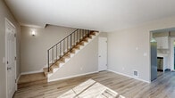 This two-story, two-bedroom, one-bathroom home is thoughtfully laid out across two well-proportioned floors. The main level features an open living room bathed in natural light from large windows, with light-toned hardwood-style flooring that runs consistently throughout the space. A sleek staircase with black metal railings serves as a subtle architectural focal point, connecting the lower and upper levels with clean, modern lines.

The combined dining room and kitchen occupies its own defined area on the main floor, featuring white shaker-style cabinetry, stainless steel appliances including a refrigerator, gas range, and dishwasher, and a sink positioned beside a window. A convenient in-unit washer and dryer closet is tucked within the kitchen area, adding practical functionality.

Upstairs, the primary bedroom offers a comfortable footprint with dual closets and a window overlooking the surroundings. The second bedroom also features natural light and ample closet storage. The full bathroom includes a tub-shower combination with tiled surround, a white vanity, and a frosted privacy window.

Throughout, the neutral warm-gray walls, crisp white trim, and consistent flooring create a cohesive and bright atmosphere. The exterior features a fenced backyard with mature greenery, offering a private outdoor retreat.