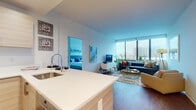 Located at 2030 Hudson St in Fort Lee, NJ, this modern residential unit offers a well-designed, open-concept single-floor layout with contemporary finishes throughout. The living area is bathed in natural light from expansive floor-to-ceiling windows that frame sweeping views of the surrounding urban skyline, creating a bright and airy ambiance. Rich hardwood-style flooring flows throughout the main living spaces, adding warmth to the clean, modern aesthetic.

The kitchen is thoughtfully designed with light wood cabinetry, stainless steel appliances including a side-by-side refrigerator, electric range, and microwave, complemented by crisp white countertops. A peninsula with bar seating connects the kitchen seamlessly to the living area, making it ideal for entertaining.

The bedrooms are generously proportioned, each benefiting from large windows that continue the theme of abundant natural light and open city views. The primary bathroom features a dual-sink vanity with wood-toned cabinetry, large mirrors, soft accent lighting, and clean tile flooring, offering a calm, spa-like atmosphere.

Throughout the unit, a cohesive, contemporary design palette of whites, neutrals, and natural wood tones creates a polished and inviting living environment in the heart of Fort Lee.