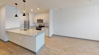 Located at 1525 N Main Street in Marion, Indiana, this thoughtfully designed single-floor residence offers a clean, contemporary aesthetic throughout. The open-concept kitchen and living area serves as the heart of the unit, featuring light wood-look vinyl flooring, white cabinetry, and striking granite countertops that extend across both the island and main cooking surfaces. The kitchen island includes an undermount sink with a modern faucet and is accented by stylish pendant lighting overhead. Stainless steel appliances — including a refrigerator, range, and microwave — complete the kitchen's polished, functional look. The adjacent living area provides an open, versatile space with a bright, neutral palette. The bedroom is generously sized with plush wall-to-wall carpeting, a ceiling fan with light fixture, and a window with blinds that allows natural light to fill the room. A dedicated walk-in closet off the bedroom offers excellent storage capacity. The bathroom is finished with the same attention to detail, featuring granite countertops on the vanity with an undermount sink, a full soaking tub with shower, wood-look flooring, and clean white walls. Throughout the space, consistent finishes and neutral tones create a cohesive, move-in-ready environment.
