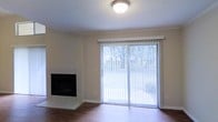 This 2-floor space offers a well-appointed living area characterized by warm hardwood flooring and a neutral color palette that creates a clean, inviting atmosphere. The living room serves as a central gathering space, highlighted by a tile-surround fireplace that adds both a functional and aesthetic focal point to the room. A large sliding glass door fitted with vertical blinds allows abundant natural light to fill the space while providing direct access to an outdoor area, where mature trees are visible, offering a pleasant natural backdrop. The textured ceiling adds subtle architectural detail, and the room's layout provides ample open space for flexible furniture arrangement. The overall ambiance of the main living area is bright and airy, with the combination of natural light, hardwood floors, and the fireplace contributing to a comfortable and practical living environment. Spanning two floors, the property offers additional living space beyond the main level, allowing for separated living and private areas throughout.