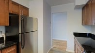 This single-floor residence offers a practical and well-maintained living environment with a clean, neutral aesthetic throughout. The kitchen is equipped with a full-size stainless steel refrigerator and warm-toned wood cabinetry, providing ample storage and a classic look. The walls are finished in a soft grey tone, lending a calm and modern feel to the space. Light-colored hardwood flooring runs throughout, adding warmth and continuity between rooms. A wide, open doorway connects the kitchen to an adjoining room, allowing natural light to flow freely and creating a sense of openness despite the compact layout. Crown molding along the upper trim adds a subtle architectural detail that elevates the overall finish of the interior. The space is thoughtfully arranged to maximize functionality on a single level, making movement between areas easy and intuitive. The overall ambiance is tidy, understated, and move-in ready, suited for those seeking a straightforward and comfortable living environment.