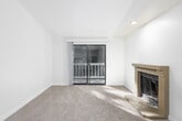 This single-floor residence offers a thoughtfully designed layout with a clean, neutral aesthetic throughout. The spacious living room serves as the heart of the home, anchored by a tiled fireplace and sliding glass door that opens to a private balcony with lush green views, allowing natural light to fill the carpeted space. Adjacent to the living area, a galley-style kitchen features white cabinetry, light-toned countertops, and light wood-look flooring, with appliances including an electric range and dishwasher. The bedrooms are generously sized with plush carpeting and windows fitted with blinds that frame verdant outdoor scenery; baseboard heaters provide efficient warmth throughout. A lower-level area offers additional flexible living space, complete with recessed lighting, carpeted flooring, a built-in shelf, and a compact refrigerator, making it well-suited as a studio, office, or recreation room. The full bathroom is finished in crisp white tones with a shower-tub combination, a vanity with mirror, and wood-look flooring. The overall ambiance is bright, clean, and move-in ready, with a consistent neutral palette that provides a versatile canvas for any décor style.