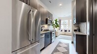 Located at 1425 Winnifred Street in Charlotte's South End neighborhood, this single-floor residence offers a thoughtfully designed open layout with contemporary finishes throughout. The galley-style kitchen is a standout feature, equipped with full stainless steel appliances including a French door refrigerator, gas range, built-in microwave, and dishwasher. Dark wood cabinetry with matte black hardware, granite countertops, and a striking hexagonal tile backsplash give the kitchen a polished, modern aesthetic. Light wood-tone flooring runs throughout the space, creating a seamless visual flow. The open living and sleeping area is bright and airy, benefiting from large windows that invite natural light and offer views of the surrounding urban streetscape. The bedroom area comfortably accommodates a full-sized bed and additional seating, making efficient use of the open floor plan. The bathroom continues the design language of the rest of the unit, featuring a dark wood vanity with granite countertop, framed mirror, globe pendant lighting, and a walk-in shower. Upper cabinetry provides additional storage. The overall ambiance is clean, modern, and urban — well-suited for those seeking a stylish, low-maintenance living space in one of Charlotte's most walkable and vibrant neighborhoods.