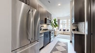 Located at 1425 Winnifred Street in Charlotte's South End neighborhood, this single-floor residence offers a thoughtfully designed open layout with contemporary finishes throughout. The galley-style kitchen is a standout feature, equipped with full stainless steel appliances including a French door refrigerator, gas range, built-in microwave, and dishwasher. Dark wood cabinetry with matte black hardware, granite countertops, and a striking hexagonal tile backsplash give the kitchen a polished, modern aesthetic. Light wood-tone flooring runs throughout the space, creating a seamless visual flow. The open living and sleeping area is bright and airy, benefiting from large windows that invite natural light and offer views of the surrounding urban streetscape. The bedroom area comfortably accommodates a full-sized bed and additional seating, making efficient use of the open floor plan. The bathroom continues the design language of the rest of the unit, featuring a dark wood vanity with granite countertop, framed mirror, globe pendant lighting, and a walk-in shower. Upper cabinetry provides additional storage. The overall ambiance is clean, modern, and urban — well-suited for those seeking a stylish, low-maintenance living space in one of Charlotte's most walkable and vibrant neighborhoods.