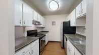 This single-floor unit offers a practical and well-organized layout across its living spaces. The living room is the largest area of the unit, featuring neutral-toned carpet, a textured ceiling, a ceiling fan, and a sliding glass door fitted with vertical blinds that allows natural light to filter in. An open pass-through connects the living room to the kitchen, maintaining a sense of visual continuity between the two spaces.

The galley-style kitchen is efficiently designed with stainless steel appliances, including an electric range and refrigerator, complemented by a dishwasher. White cabinetry lines both sides of the kitchen, providing ample storage, while dark granite-style countertops add contrast. Warm hardwood-style flooring runs throughout the kitchen, and a flush-mount ceiling light provides functional illumination.

The bedroom is a generously sized room with carpeted floors, neutral walls, a textured ceiling, and a window that brings in natural light. A hallway with carpeted floors connects the main living areas to the two bathrooms, each featuring a full bathtub and shower combination with white tile surround and chrome fixtures. One bathroom includes hardwood-style flooring, while both maintain a clean, utilitarian aesthetic throughout.