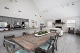 Located at 3321 N Hills St in Meridian, Mississippi, this single-story home showcases a thoughtfully designed open-concept floor plan united by dramatic vaulted ceilings that lend an impressive sense of height and airiness throughout the main living areas. The living room serves as the heart of the home, anchored by a striking whitewashed brick fireplace with a rustic wood mantel and a curved hearth surround. Track lighting along the ceiling beam highlights the soaring roofline, while multiple windows and French doors flood the space with natural light and provide access to the outdoors. Light hardwood-style flooring flows seamlessly across the main areas, complementing the neutral gray wall palette. The kitchen features dark granite countertops, gray cabinetry, stainless steel appliances, and a breakfast bar with barstool seating — ideal for casual dining or entertaining. Adjacent to the kitchen, a spacious dining area accommodates a large farmhouse-style table and benefits from windows on multiple walls, ensuring bright, well-lit meals. A dedicated office nook with high vaulted ceilings offers a quiet workspace. The overall ambiance is bright, open, and contemporary, with architectural details that elevate the character of this well-appointed single-floor home.