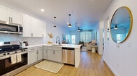 Located at 5815 S Elk Way in Aurora, CO, this well-appointed one-bedroom, one-bathroom residence delivers a thoughtfully designed open-concept layout across a single floor. Light wood-tone flooring flows throughout, anchoring the bright, neutral color palette that defines the space.

The kitchen is a standout feature, showcasing two-tone cabinetry — crisp white uppers paired with sage-gray lowers — complemented by a hexagonal tile backsplash, white quartz countertops, and a full suite of stainless steel appliances including a gas range, microwave, refrigerator, and dishwasher. Stylish pendant lights hang above the peninsula, which transitions seamlessly into the living area.

The living room is generously proportioned, bathed in natural light from large windows with sheer draping curtains, and finished with a ceiling fan overhead. A private exterior door adds convenient outdoor access.

The bedroom is a calm, sunlit retreat with a window overlooking the exterior and light hardwood flooring. The bathroom features large-format gray tile wall cladding, a lighted vanity mirror, soft-close cabinetry, and wood-look flooring for a spa-like feel.

A dedicated laundry room with a full-size washer and dryer and additional closet storage complete this functional and contemporary home.