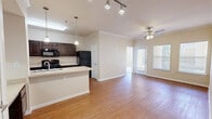 This single-floor, 2-bedroom, 2-bathroom residence offers a practical and comfortable layout designed for everyday living. The open-concept main area seamlessly connects the kitchen, dining, and living spaces, all finished with warm hardwood-style flooring. Crown molding adds a refined touch, while a ceiling fan and access to a private exterior door enhance the living room's comfort and functionality. Natural light flows in through multiple windows fitted with blinds.

The kitchen is a standout feature, showcasing rich dark wood cabinetry, light countertops, a peninsula with pendant lighting, and black appliances including a refrigerator, range, microwave, and dishwasher. A dedicated pantry provides additional storage, and a built-in shelving nook adds further organizational versatility.

Both bedrooms are carpeted and receive natural light through sizable windows. The primary bedroom connects to a well-sized walk-in closet outfitted with wire shelving systems on multiple walls. The two bathrooms are thoughtfully appointed—one features a tiled shower/tub combo with a dark wood vanity, and the other includes a walk-in shower visible in the mirror reflection. Four total closets throughout the unit offer exceptional storage capacity for a residence of this size.