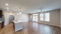 This well-appointed single-floor residence offers a thoughtfully designed open-concept layout that seamlessly connects the kitchen, dining, and living areas. The living space is finished with warm hardwood-style flooring and features a ceiling fan, recessed track lighting, and generous natural light streaming through large windows and glass French doors that open to the outdoors.

The kitchen is a standout feature, showcasing rich dark espresso cabinetry that reaches to the ceiling, a classic tile backsplash, white quartz countertops, and a full suite of stainless steel appliances including a side-by-side refrigerator with ice dispenser, electric range, and built-in microwave. A central island with an undermount sink and pendant globe lighting provides both additional prep space and a casual dining option.

The bedroom is carpeted for comfort and includes a ceiling fan, a window with natural views, and ample closet space. The bathroom is clean and contemporary, featuring dark cabinetry, a white quartz vanity, and a full tub and shower combination with large-format tile surround. A dedicated in-unit laundry area houses a full-size side-by-side washer and dryer with built-in shelving above. The overall aesthetic is modern and neutral, with a cohesive palette of warm tones throughout.