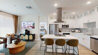 This thoughtfully designed 2-bedroom, 1-bathroom single-floor residence offers a functional and stylish layout centered around an impressive open-concept kitchen. The kitchen is a standout feature, showcasing white shaker-style cabinetry extending to the ceiling with frosted glass upper panels, a light quartz countertop island with a built-in gas cooktop, a sleek stainless steel island range hood, subway tile backsplash, and a full suite of stainless steel appliances including a French door refrigerator, built-in microwave, wall oven, and dishwasher. The island doubles as a breakfast bar with seating, flowing naturally into the adjacent dining and living areas. Light wood-tone flooring runs throughout, lending warmth and continuity to the open layout. The primary bedroom features a sliding glass door that opens to a private balcony, filling the room with natural light and outdoor views. The second bedroom is cozy and well-proportioned, with a barn-style sliding door adding a contemporary architectural touch. Both bedrooms are served by two closets. The bathroom includes a full soaking tub with shower combo and clean white tile finishes. A connecting hallway ties the layout together efficiently, completing this compact yet well-equipped residence.