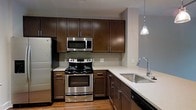 Situated at 650 Enterprise Blvd in Charleston, South Carolina, this single-floor space offers a thoughtfully designed layout with modern finishes throughout. The kitchen serves as a central highlight, showcasing rich dark-brown cabinetry that extends floor to ceiling, providing ample storage and a sleek, contemporary aesthetic. Crisp white quartz countertops contrast beautifully with the warm cabinetry tones, while a full suite of stainless steel appliances — including a refrigerator, range with oven, built-in microwave, and undermount sink with a modern arc faucet — ensures both functionality and style. A decorative pendant light hangs above the countertop, adding a refined touch to the kitchen's ambiance. The backsplash features subtle, neutral tiling that complements the overall color palette. Light hardwood flooring runs through the space, contributing warmth and continuity. The open design of the kitchen allows for a natural flow into the adjoining living areas, making the layout well-suited for both everyday living and entertaining. Neutral-toned walls throughout keep the space feeling bright and versatile, ready to accommodate a range of interior styles.