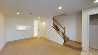 This two-floor residence offers a practical and comfortable layout across both levels. The main living area is bright and open, finished with plush wall-to-wall carpeting and recessed lighting. A classic staircase with a warm wood banister and white spindles connects the two floors, adding a traditional architectural touch. The kitchen is well-equipped, featuring warm honey-toned wood cabinetry, white appliances including an electric range, built-in microwave, dishwasher, and a full-size refrigerator. Light countertops provide ample workspace, and a pass-through window connects the kitchen to the adjacent living area, enhancing the sense of openness. The bedroom offers generous space with natural light flowing in through multiple windows dressed with horizontal blinds. A standout feature is the dual closet configuration, providing abundant storage with full-length hanging rods. Baseboard heating is present throughout the upper level. The full bathroom is clean and functional, complete with a wood vanity, white countertop, tiled tub-shower combination, and light tile flooring. Recessed lighting and neutral white walls throughout the home create a bright, move-in-ready atmosphere suited for a variety of living arrangements.