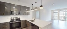 Located at 3718 University Dr in Durham, NC, this single-floor unit showcases a contemporary design with carefully selected finishes throughout. The kitchen serves as a central highlight, featuring high-gloss dark cabinetry accented with gold hardware, a full suite of stainless steel appliances, and a crisp white subway tile backsplash. A generous peninsula island with a white quartz countertop and undermount sink fitted with a brushed gold faucet provides additional workspace and casual seating. Globe pendant lights suspended overhead add a modern, stylish touch.

Light wood-style flooring extends through the kitchen and main living areas, creating a warm, cohesive aesthetic. The bedrooms are carpeted for comfort and each include a ceiling fan with recessed lighting, as well as windows fitted with blinds that allow natural light. The bathrooms are finished with granite countertops, dark-framed cabinetry, matte black fixtures, and bold framed mirrors. Each bathroom is positioned adjacent to a walk-in closet with wire shelving, offering practical storage. The overall ambiance is clean, modern, and move-in ready.