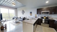 This 2-bedroom, 1-bathroom unit is thoughtfully designed with a modern, open-concept layout that seamlessly connects the kitchen and living areas. The kitchen is outfitted with dark espresso cabinetry, granite countertops, a peninsula with a stainless steel sink, and stainless steel appliances including a microwave, electric range, and dishwasher. The peninsula serves as a natural divider between the kitchen and the living space while keeping the floor plan open and airy. The living area features polished concrete flooring that extends throughout, contributing to the unit's contemporary industrial aesthetic. A slatted wood-panel ceiling accent adds architectural character and visual warmth to the space. Large windows invite an abundance of natural light and offer views of the surrounding landscape, enhancing the bright and welcoming ambiance. The neutral color palette throughout the space, paired with clean lines and modern fixtures, creates a cohesive and functional environment. The single-floor layout ensures ease of navigation, making this a practical and stylish living space suited for a variety of lifestyles.