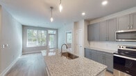 Located at 5701 Glenwood Ave in Raleigh, NC, this single-floor residence offers a thoughtfully designed layout with modern finishes throughout. The kitchen serves as the heart of the home, showcasing floor-to-ceiling gray shaker-style cabinetry, light granite countertops, a large center island with an undermount sink and pendant lighting, and a full suite of stainless steel Whirlpool appliances including a refrigerator with ice maker, electric range, and over-the-range microwave. Light hardwood-style flooring runs throughout the kitchen and living areas, complementing the clean, neutral color palette. The living and dining area flows naturally from the kitchen and benefits from multiple windows that invite abundant natural light and views of surrounding greenery. The bedrooms feature plush carpeting and well-sized windows with views of the tree-lined exterior, creating a calm and comfortable atmosphere. The bathrooms are finished with the same granite vanity tops, dark cabinetry, and light wood-style flooring. One bathroom includes a tub-shower combination with marble-style tile surround, while another features a glass-enclosed shower. The overall design emphasizes a cohesive, contemporary aesthetic with neutral tones, quality materials, and an abundance of natural light throughout.