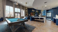 This single-floor amenity lounge is a thoughtfully designed social hub that blends modern aesthetics with a range of recreational and functional spaces. Throughout the space, warm herringbone-patterned hardwood flooring ties together each distinct area, while soaring ceilings and floor-to-ceiling arched windows flood the interior with natural light and offer views of the surrounding exterior.

The main lounge area makes an immediate impression with its dramatic scale, featuring bold navy blue accent walls, textured wallcoverings, and an array of striking gold sputnik chandelier pendants that add a retro-modern flair. A full-size billiards table anchors the game area, complemented by an arcade cabinet tucked into a nearby nook. Comfortable lounge seating in deep blues and whites encourages casual gatherings, while a cozy fireplace with a stone surround provides a warm focal point.

The kitchen area is fully equipped with deep navy cabinetry, a mosaic tile backsplash, stainless steel appliances including a full-size refrigerator and double wall oven, and a large white island with counter seating. A separate glass-partitioned workspace offers a quieter environment with workstations and ample desk space. Bold abstract artwork and lush tropical plants are featured throughout, completing the vibrant, curated ambiance of this exceptional communal space.