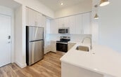 Located at 27077 S Dixie Hwy in Homestead, FL, this 2-bedroom, 1-bathroom unit offers a thoughtfully designed open-concept layout with clean, modern finishes throughout. Warm wood-look flooring flows seamlessly across the living, dining, and kitchen areas, creating a cohesive and inviting atmosphere. The kitchen is a standout feature, outfitted with crisp white shaker cabinetry extending to the ceiling, stainless steel appliances including a refrigerator, range, and microwave, a single-basin sink, and light quartz countertops. A peninsula with pendant lighting connects the kitchen to the open living area, enhancing both functionality and style. The primary bedroom is a comfortable retreat featuring sliding glass doors that open to a private balcony with scenic views of the surrounding Homestead area, complemented by a ceiling fan. The second bedroom includes a built-in closet and a window that brings in natural light and outdoor views. The bathroom is finished with large-format white wall tiles, a frameless sliding glass shower enclosure, a floating vanity, and clean, modern fixtures. A hallway connects the living spaces to the bedrooms and bathroom, keeping the layout organized and efficient. The unit's bright white walls and natural light create an airy, contemporary ambiance throughout.