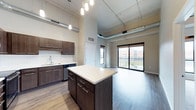 This single-floor space showcases an open-concept layout that seamlessly connects the kitchen and living areas. The kitchen is outfitted with dark espresso cabinetry, a white subway tile backsplash, stainless steel appliances, and a central island with a light-toned countertop and built-in storage — ideal for both cooking and casual dining. Pendant lighting hangs above the island, adding focused illumination and a modern aesthetic touch.

The soaring ceilings are a defining architectural feature, amplifying the sense of openness throughout. Exposed ductwork runs along the upper portion of the space, lending an industrial character that complements the contemporary finishes. Hardwood-style flooring extends across the entire unit, providing a warm, cohesive foundation.

The living area benefits from abundant natural light, courtesy of large sliding glass doors and adjacent windows that open to a private balcony with metal railings and views of the surrounding exterior. The balcony access enhances the indoor-outdoor connection and brings in a strong sense of openness. Overall, the space combines modern finishes with industrial design elements for a stylish, functional environment.