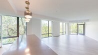 Located at 17 Ridge Square NW in Washington, DC, this thoughtfully designed 3-bedroom, 2-bathroom residence offers a bright, contemporary living experience across a single, well-organized floor. The open-plan kitchen and living area serves as the heart of the home, where expansive floor-to-ceiling windows flood the space with natural light and frame verdant tree canopy views. The sleek, modern kitchen features flat-front cabinetry, an induction cooktop, built-in wall ovens, an undermount sink, and a generous island with a waterfall countertop, all illuminated by a sculptural pendant light. Light hardwood flooring flows seamlessly throughout the living areas and bedrooms, reinforcing the home's clean, minimalist aesthetic. The three bedrooms are well-proportioned, with the primary suite offering generous closet space. Both bathrooms are finished in neutral tile, with floor-to-ceiling windows, floating vanities, and soaking tubs or glass-enclosed showers. A dedicated laundry room houses a stacked washer and dryer unit. A private balcony extends the living space outdoors. The long, clean hallway connects each room with a sense of openness and order, completing this refined and functional Washington, DC residence.
