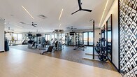 Located at 321 Main St in Hackensack, NJ, this expansive fitness center offers a generously sized, single-floor exercise space thoughtfully designed for a comprehensive workout experience. The facility features a clean, modern aesthetic with white walls, linear recessed lighting, and multiple ceiling fans that contribute to a bright, well-ventilated atmosphere throughout.

The space is divided into distinct functional zones. A dedicated cardio area lines the perimeter, equipped with treadmills, elliptical machines, stair climbers, stationary bikes, and rowing machines, all positioned to take advantage of large floor-to-ceiling windows that flood the room with natural light and offer open outdoor views. A strength training zone houses a robust selection of cable machines, multi-functional cable towers, and adjustable benches, complemented by a well-stocked free weights area featuring dumbbells, kettlebells, medicine balls, stability balls, and weight plates on vertical racks.

A separate functional training zone is outfitted with a dedicated storage rack for accessories including TRX suspension straps and resistance equipment. Full-length mirrors are strategically placed throughout, enhancing the sense of space. The flooring transitions between resilient rubber and smooth hardwood-style surfaces to suit different training needs. A storage credenza and decorative wall art add a polished, hospitality-inspired finish to the space.