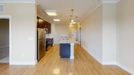 Located at 100 Holling FR in Frederick, Maryland, this single-floor residence offers a thoughtfully designed layout with a warm, neutral color palette throughout. The open-concept kitchen is a standout feature, showcasing rich dark cabinetry, stainless steel appliances including a gas range and refrigerator, granite countertops, a classic subway tile backsplash, and a large center island with pendant lighting overhead. Crown molding and light hardwood flooring add a polished finish to the kitchen and adjoining living areas. The living room is generously sized, bathed in natural light from multiple windows and a glass door that opens to an outdoor balcony, offering pleasant exterior views. Bedrooms are carpeted for comfort, each featuring ample closet space with white panel doors. One bedroom includes a double-door closet, while another offers direct hallway access. The full bathroom is finished with white tile surrounding the tub-shower combination, a dark wood vanity, and a large mirror. A second half-bath provides additional convenience, featuring a vanity, support bar, and light tile flooring. The space maintains a clean, contemporary ambiance suitable for everyday living.