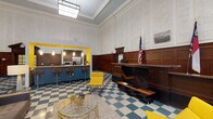 Located on North Main Street in downtown Winston-Salem, this single-floor space occupies a strikingly preserved historic building that masterfully blends classical architecture with contemporary design. The grand interior is defined by soaring ceilings adorned with ornate crown molding and intricate textured wall panels, complemented by rich, dark wood wainscoting that lines the walls throughout. A signature teal-and-cream checkerboard tile floor anchors the entire space, creating a bold visual continuity from room to room.

The main lounge area features a modern fireplace set against a teal accent wall, a cozy seating arrangement with mid-century inspired furniture, and vibrant yellow accent chairs that punctuate the space with energy. A fully equipped kitchen with bar seating is framed by a bold yellow archway, offering stainless steel appliances and pendant lighting. Glass-partitioned walls reveal an interior fitness area with cardio equipment, maintaining openness while defining distinct zones. A recreation area accommodates a ping-pong table alongside casual seating, adding a social, active dimension to the space. Classical doorways with pediment detailing and multi-pane glass panels further underscore the building's historic character, while curated artwork and an American flag add personality and civic pride throughout.