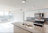 Located at 2610 109 Street NW in Edmonton, Alberta, this modern one-bedroom, one-bathroom unit offers a thoughtfully designed layout across a single floor. Light wood-look flooring runs throughout, complementing a clean, neutral palette that creates a bright and airy atmosphere.

The open-concept kitchen is a standout feature, equipped with stainless steel appliances including a French door refrigerator, electric range, and built-in microwave. Two-tone cabinetry pairs white upper cabinets with warm wood-grain lower cabinets, accented by a geometric herringbone tile backsplash and sleek dark countertops. A central island with a double sink and an integrated wine rack adds both functionality and style, flowing naturally into the living area.

Floor-to-ceiling windows in the living space and bedroom fill the unit with abundant natural light and offer expansive views of the Edmonton skyline — a defining feature of this high-floor residence. The bedroom is a comfortable retreat with light-filled windows and the convenience of two closets, providing ample storage.

The bathroom includes a full soaker tub and shower combination with clean white finishes. Additional features include in-unit laundry and two closets. This well-appointed unit combines modern finishes with practical design elements throughout.