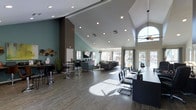 This single-floor space is defined by its striking vaulted ceiling, which rises dramatically to create an open, airy atmosphere throughout the main area. Recessed lighting is distributed generously across the ceiling, complementing the natural light that streams in through a large arched window and a wall of French doors along the rear. The flooring features wood-look tile in a warm, neutral tone, adding texture and cohesion across the expansive open-plan layout. The space is divided into distinct functional zones. A lounge area toward the rear is furnished with contemporary gray sofas and accent chairs arranged around a central rug, creating a comfortable gathering spot. Toward the front, high-top tables paired with bar-height stools offer a casual seating option. A flat-screen television is mounted on the wall, adding to the amenity-style feel of the space. Teal-painted accent walls contrast with the white ceiling and neutral flooring, providing a modern, welcoming color palette. Decorative elements, including wall-mounted metallic accents and potted greenery, add personality throughout. The French doors along the back wall offer views and access to an outdoor area, enhancing the connection between interior and exterior spaces.