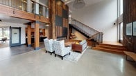 Located at 259 Ferncliff Ave NE on Bainbridge Island, WA, this single-floor commercial space delivers a compelling blend of modern industrial design and warm, natural materials. Soaring ceilings and expansive floor-to-ceiling windows flood the open-plan interior with natural light and offer views of the surrounding Pacific Northwest landscape. Polished concrete floors run throughout the main areas, lending a sleek, cohesive feel to the space.

The fully equipped kitchen features a striking subway tile backsplash, dark wood cabinetry, open shelving, stainless steel appliances, a gas range, and a large central island with bar seating — ideal for community gatherings or catered events. Adjacent to the kitchen, a spacious dining area accommodates a live-edge wood table beneath contemporary pendant lighting, with glass doors opening to an outdoor patio.

A dedicated conference room showcases a reclaimed wood accent wall, exposed wood beam ceiling detail, and a long live-edge conference table with ample seating, supported by a wall-mounted display and natural outdoor views. Separate lounge areas offer flexible seating arrangements, including a fireplace lounge with a full-height tile surround. Throughout, design details such as exposed brick, barn-style sliding doors, heavy timber columns, and reclaimed wood accents create a warm yet refined ambiance suited for professional or community use.