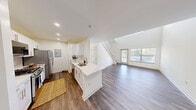 Located at 1 Avalon Drive in Hull, MA, this two-story, two-bedroom, two-bathroom home offers a well-designed layout spread across two floors. The spacious main floor serves as the heart of the home, anchored by an open-concept kitchen and living area filled with natural light from large windows and a glass entry door. The kitchen features white shaker cabinetry, quartz countertops with a waterfall-edge peninsula, a stainless steel sink, gas range, and a stainless steel refrigerator — all complemented by recessed lighting and hardwood-style flooring that flows throughout the main level. A carpeted staircase with a white balustrade connects to the upper floor, where the two bedrooms are located. The primary bedroom is a comfortable retreat with high ceilings, hardwood-style flooring, and natural light. Both bathrooms are finished with quartz vanity tops and hardwood-style flooring; one features a full tub-shower combination with tile surround, while the other includes a wide vanity with a large mirror. A dedicated laundry room with a full-size washer and dryer adds everyday convenience. Three closets and two hallways provide ample storage throughout the home.