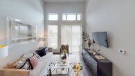 Metro 22 presents a thoughtfully designed single-floor residence that balances contemporary aesthetics with functional living. The space is characterized by notably tall ceilings throughout, which amplify the sense of openness and allow natural light to penetrate deep into the interior through strategically placed clerestory windows and full-height glazing.

The living area serves as the centerpiece of the unit, featuring soaring ceilings, dark hardwood-style flooring, and a generous wall of windows topped with transom panes that flood the room with natural light. A sliding glass door provides outdoor access and adds to the airy atmosphere.

The kitchen is outfitted with flat-front cabinetry in a warm wood-tone finish, white quartz countertops, a mosaic tile backsplash with under-cabinet lighting, and a full suite of stainless steel appliances, including a French-door refrigerator and over-range microwave.

The bedrooms offer a calm retreat, with one accessed via a sliding barn door that opens into a well-sized bathroom featuring wood-tone vanity cabinetry, a vessel sink, large-format tile flooring, and a separate water closet. A second bathroom includes a tub-shower combination with floor-to-ceiling tile surround. Throughout, the design maintains a cohesive modern aesthetic with neutral tones and clean lines.