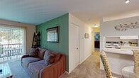 This single-floor residence offers a thoughtfully arranged layout that balances comfort and functionality. The living room serves as the heart of the space, distinguished by a striking green accent wall that adds a vibrant focal point to the otherwise neutral palette. Plush wall-to-wall carpeting runs throughout the main living and sleeping areas, contributing to a warm, cozy atmosphere. A sliding glass door in the living room opens directly onto a private balcony, allowing natural light to pour in and offering pleasant outdoor views of surrounding greenery.

Adjacent to the living room, the galley-style kitchen is efficiently designed with white cabinetry lining both walls, providing ample storage. Light-toned countertops, tile flooring, and white appliances create a clean, bright workspace.

A hallway connects the living areas to the bedroom, which is generously proportioned and features a window with views of mature trees, further enhancing the sense of calm. The room accommodates substantial furniture comfortably and benefits from soft natural light.

The bathroom is finished with a large vanity mirror, a wide countertop with an integrated sink, and light-toned walls that keep the space feeling open and airy. Overall, the residence presents a cohesive, functional living environment with distinctive design accents throughout.
