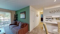 This single-floor residence offers a thoughtfully arranged layout that balances comfort and functionality. The living room serves as the heart of the space, distinguished by a striking green accent wall that adds a vibrant focal point to the otherwise neutral palette. Plush wall-to-wall carpeting runs throughout the main living and sleeping areas, contributing to a warm, cozy atmosphere. A sliding glass door in the living room opens directly onto a private balcony, allowing natural light to pour in and offering pleasant outdoor views of surrounding greenery.

Adjacent to the living room, the galley-style kitchen is efficiently designed with white cabinetry lining both walls, providing ample storage. Light-toned countertops, tile flooring, and white appliances create a clean, bright workspace.

A hallway connects the living areas to the bedroom, which is generously proportioned and features a window with views of mature trees, further enhancing the sense of calm. The room accommodates substantial furniture comfortably and benefits from soft natural light.

The bathroom is finished with a large vanity mirror, a wide countertop with an integrated sink, and light-toned walls that keep the space feeling open and airy. Overall, the residence presents a cohesive, functional living environment with distinctive design accents throughout.