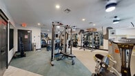 Located at 10480 Auto Mall Pkwy in D'Iberville, Mississippi, this fitness center offers a generously sized, single-floor workout space designed to accommodate a full range of exercise needs. The layout is thoughtfully organized, with distinct zones for strength training and cardiovascular equipment, allowing for efficient use of the floor area.

The strength training section is well-appointed with multiple cable machines, a power rack, a functional trainer, and a variety of selectorized weight machines targeting different muscle groups. A dedicated dumbbell rack provides additional free weight options. The cardio zone features treadmills, ellipticals, a stair climber, and stationary bikes, offering ample variety for aerobic workouts.

Flooring transitions between light vinyl and teal-toned carpet tiles, visually defining the different workout zones. Large mirrors line the walls, enhancing the sense of openness and allowing users to monitor their form. An eye-catching abstract mural in warm neutral tones adds a modern, energetic aesthetic to the space.

Ceiling fans and recessed lighting provide consistent air circulation and bright, even illumination throughout. Windows along the perimeter allow natural light to filter in. Built-in shelving offers convenient storage, and the overall design maintains a clean, contemporary ambiance suited to a productive fitness experience.