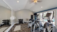 Located at 2181 Dunlap St in North Charleston, SC, this single-story fitness center is thoughtfully designed to support a well-rounded workout routine. The space features vaulted ceilings with recessed lighting and ceiling fans, creating an open, airy atmosphere that feels welcoming and comfortable. The interior is finished with a combination of cool gray and bold blue accent walls, complemented by patterned carpet tile flooring that adds visual texture throughout.

The cardio zone is well-equipped with multiple treadmills, elliptical machines, and a stationary bike, all positioned to take advantage of the abundant natural light streaming in through large windows and glass-panel doors. A wall-mounted television provides entertainment during workouts. The strength and free weight area includes a full rack of dumbbells and kettlebells in various sizes, along with a weight bench and a wall-mounted resistance training mat.

A built-in water fountain offers convenient hydration access. The space benefits from direct access to an outdoor pool area through glass French doors, providing refreshing views of the pool and patio. Additional windows along the perimeter bring in natural light from multiple directions, creating a bright and energizing environment ideal for daily fitness routines.