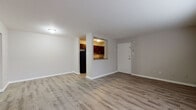 This single-floor unit is designed with a practical, straightforward layout that maximizes functionality across its living spaces. The open living area serves as the central hub of the unit, finished with light gray wood-look flooring that extends consistently throughout. Neutral-toned walls and white trim create a clean, cohesive aesthetic. A white entry door opens directly into this space, with the kitchen accessible via a half-wall pass-through opening that adds visual connectivity between the two areas.

The kitchen is compact yet well-equipped, featuring rich dark wood cabinetry with brushed silver hardware, granite-look laminate countertops, a stainless steel sink, a black gas range with overhead ventilation, and a full-size black refrigerator. White subway tile backsplash accents the cooking area.

Two bedrooms are situated toward the rear of the unit, each finished with the same wood-look flooring and neutral walls. Both rooms benefit from natural light provided by wide, horizontal windows with blinds, and each is equipped with baseboard heating units running along the exterior walls.

The bathroom features a full-size soaking tub with a white surround enclosure, accented by light blue wall tiles, a white vanity with an integrated sink, and tile flooring.