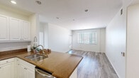 This single-story unit offers a thoughtfully designed layout across two bedrooms and two bathrooms. The open-concept living and kitchen area forms the heart of the unit, where light wood-style flooring flows seamlessly throughout. Large windows fitted with horizontal blinds fill the living room with natural light, creating a bright and welcoming atmosphere.

The kitchen is well-equipped with stainless steel appliances, including a refrigerator, range, and built-in microwave. White shaker-style cabinetry extends to the upper walls, providing ample storage, while granite-style countertops and a peninsula with a double sink offer functional workspace and casual dining potential.

The primary bedroom is generously sized, featuring large windows with outdoor views and access to a dedicated walk-in closet outfitted with multi-tiered shelving. Its ensuite bathroom includes a soaking tub with a sliding glass enclosure. The second bedroom is comfortably sized with a window providing natural light. The second bathroom mirrors a clean, modern aesthetic with a shower/tub combo and a vanity with mirror. Hallways connect all rooms efficiently, completing this well-organized floor plan.