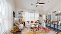 Located in Port Saint Lucie, FL, this single-story, 3-bedroom, 3-bathroom home is designed for comfortable, efficient living. The standout living room impresses with dramatic vaulted ceilings and a ceiling fan overhead, while an abundance of windows dressed in white curtains and plantation shutters floods the space with natural light. Wood-look flooring runs throughout, anchoring the bright, airy aesthetic.

The kitchen is well-appointed with gray shaker-style cabinetry, stainless steel appliances including a refrigerator, range, and built-in microwave, and clean white countertops — offering both style and functionality.

The primary bedroom is a comfortable retreat featuring a ceiling fan, natural light from a shuttered window, and a calm, neutral palette. Each of the three bathrooms is finished with gray vanity cabinetry, white countertops, and a tub-shower combination.

The exterior, visible in the dollhouse view, reveals a private enclosed patio with a green lawn area — ideal for outdoor relaxation. Two hallways connect the rooms efficiently throughout the single-level layout. The home's cohesive design, vaulted ceilings, and generous natural light create a welcoming and functional living environment.