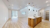 This two-story home features a thoughtfully designed layout spread across two well-proportioned floors. The main level is anchored by an open-concept kitchen and living area that immediately impresses with soaring double-height ceilings and an abundance of natural light streaming through sliding glass doors and multiple windows. The kitchen is a standout feature, showcasing a large center island with a white quartz countertop and natural wood cabinetry, complemented by white upper cabinets, a subway tile backsplash, stainless steel appliances, and a trio of stylish pendant lights overhead. Light-toned hardwood-style flooring flows throughout the main level, enhancing the bright, airy atmosphere.

The upper floor hosts the bedrooms, including a well-sized primary bedroom with a walk-in closet, all featuring plush carpeting. The open hallway overlooks the main level below, reinforcing the home's open and connected feel. Multiple windows on this level provide natural light throughout. The bathrooms are finished with clean white surrounds and matte black fixtures. A dedicated laundry room with full-size washer and dryer adds practical convenience. Overall, the home presents a clean, contemporary aesthetic with modern finishes throughout.