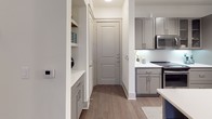 This thoughtfully designed 2-bedroom, 2-bathroom residence offers a spacious single-floor layout with contemporary finishes throughout. The open-concept kitchen serves as a central hub, featuring gray shaker-style cabinetry, stainless steel appliances, a subway tile backsplash, and a large island with a white quartz countertop and built-in sink — ideal for both cooking and casual dining. Pendant lighting and under-cabinet illumination enhance the modern aesthetic.

The living area is bathed in natural light from expansive floor-to-ceiling doors that open to an outdoor space, complemented by warm hardwood-style flooring and a ceiling fan. The primary bedroom features plush carpeting, a ceiling fan, and large windows that invite abundant natural light, while the en-suite bathroom offers a dual-sink vanity with quartz countertops, a soaking tub, and a glass-enclosed walk-in shower with tile surround. A spacious walk-in closet provides ample storage.

The second bedroom is equally comfortable, offering its own en-suite bathroom access. Additional highlights include a dedicated laundry area with built-in shelving and washer/dryer hookups, a built-in entry nook, and consistent gray-toned finishes that create a cohesive, modern atmosphere throughout.
